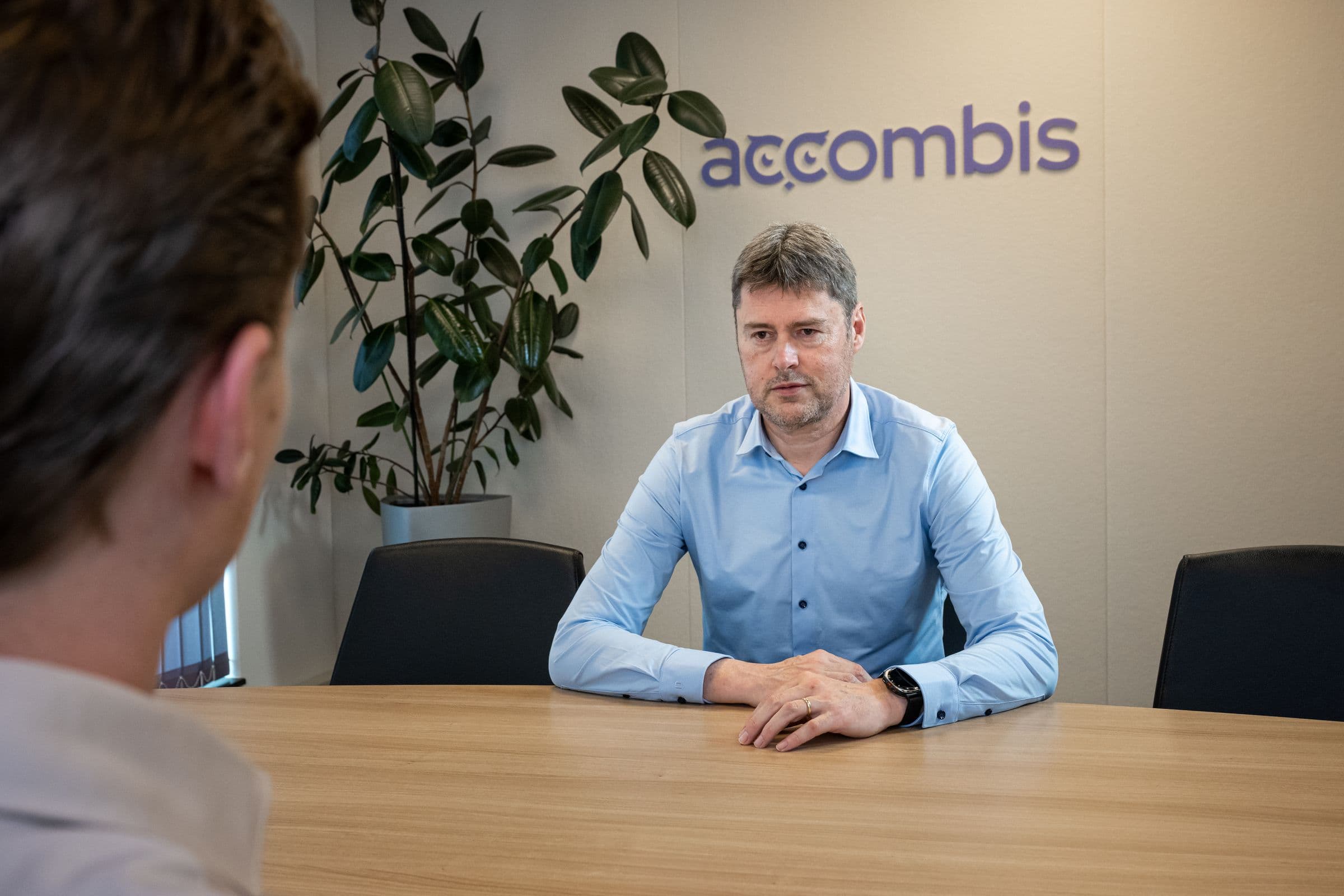 Adviseur van Accombis aan de vergadertafel, met het logo op de wand erachter
