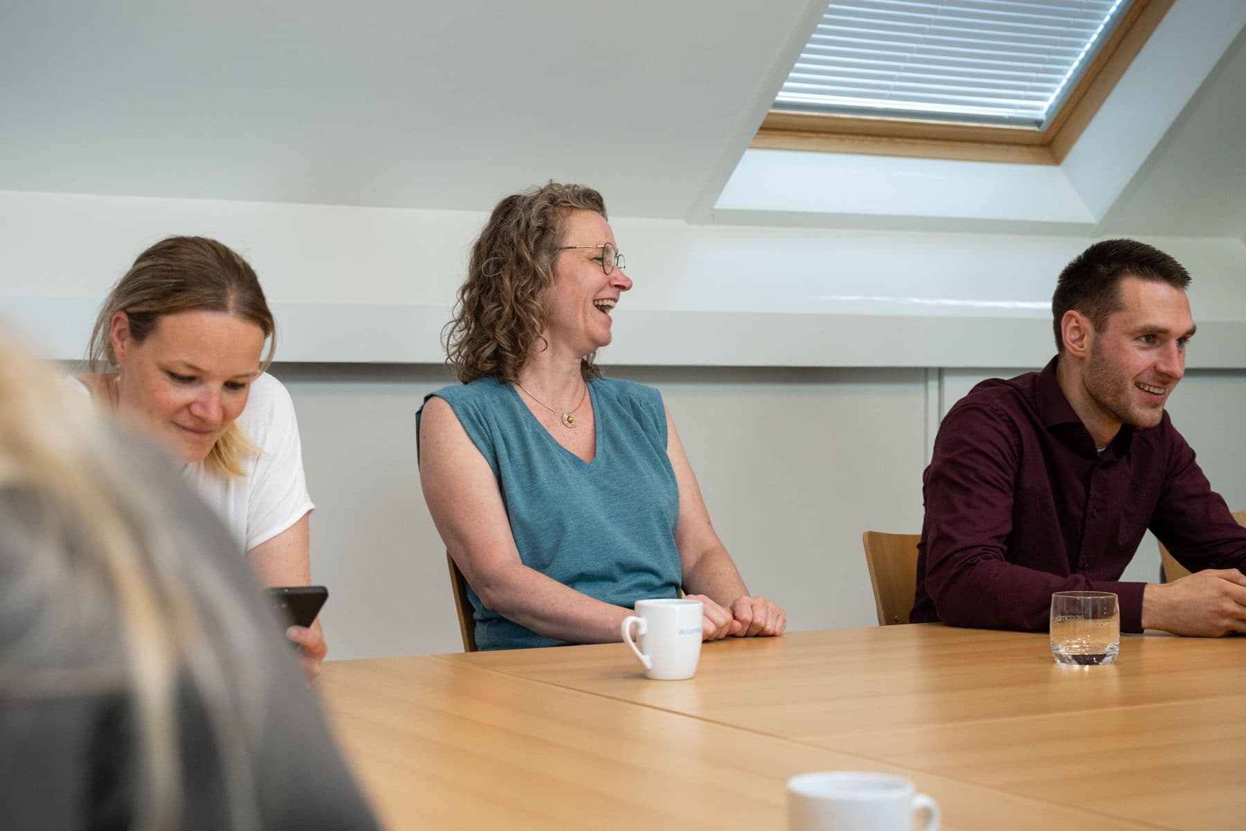 Drie collega's van Accombis lachen samen aan de vergadertafel