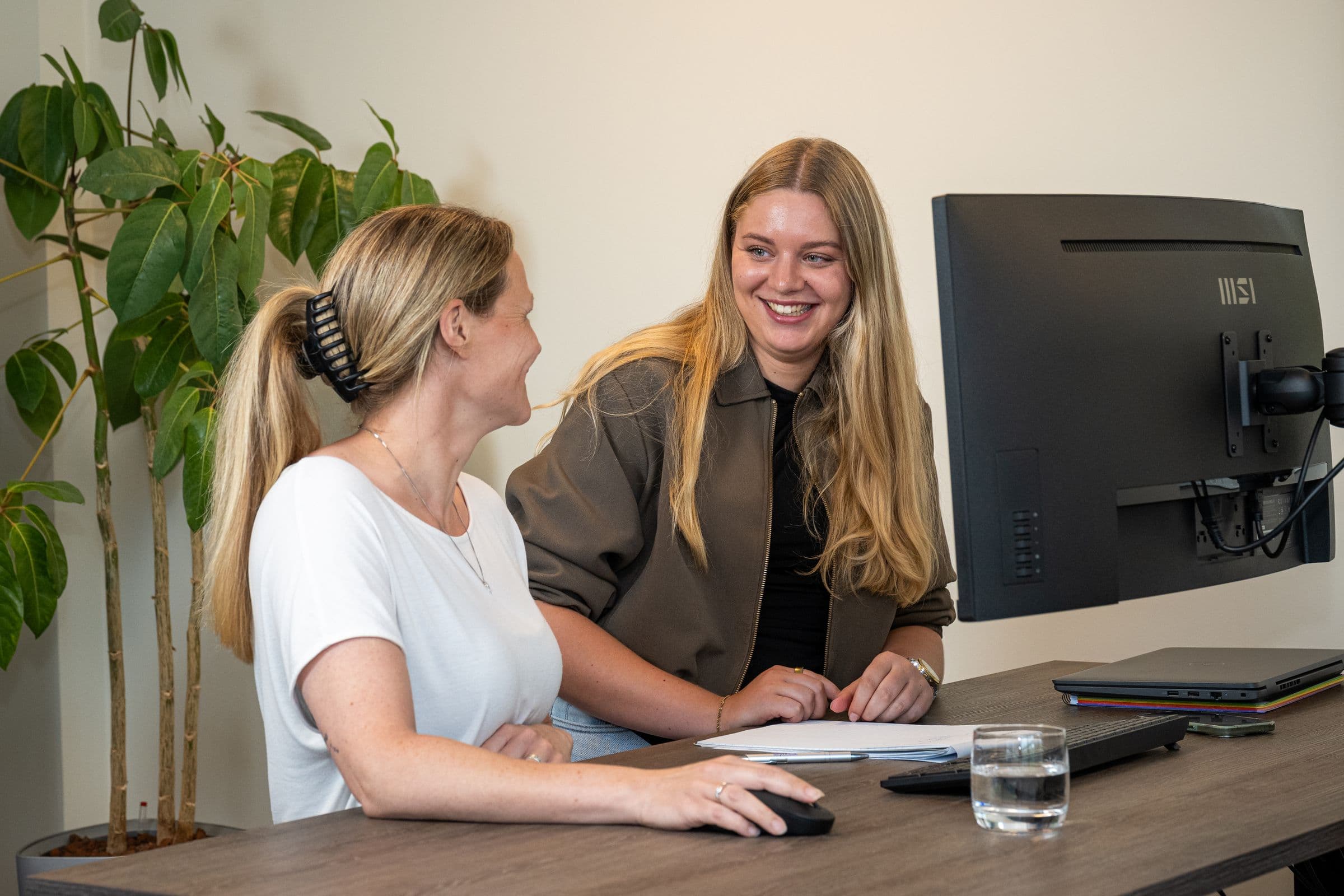 Twee collega's van Accombis lachen samen aan een bureau